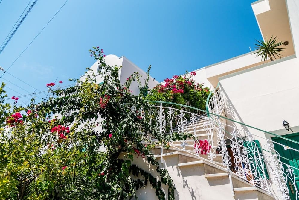 A picturesque Mediterranean staircase adorned with vibrant flowers and ornate railings under a clear blue sky, ideal for travelers seeking charming architectural details and serene photo opportunities.
