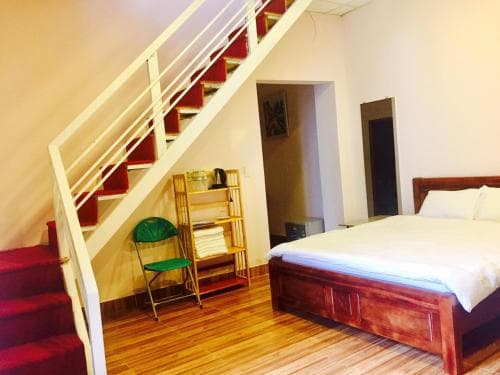 A cozy loft bedroom with a wooden bed, staircase leading to an upper level, and a small green chair, ideal for travelers seeking a compact yet charming accommodation space.