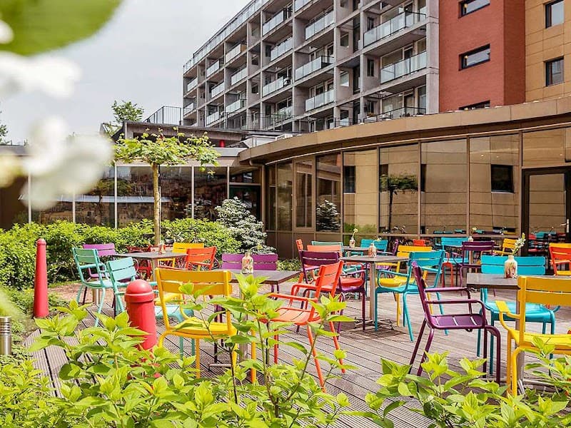 A vibrant outdoor seating area with colorful chairs and lush greenery offers a cheerful urban oasis near the Ibis Amsterdam Centre Stopera, ideal for travelers seeking relaxation in a lively city setting.