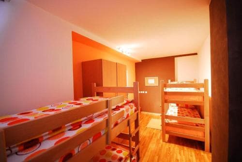A cozy hostel room with vibrant orange accents, wooden bunk beds adorned with colorful bedding, and a warm ambiance, ideal for budget travelers seeking a comfortable stay.