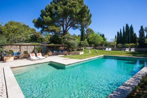 A serene outdoor oasis features a sparkling pool surrounded by lush greenery, lounge chairs, and stone walls, ideal for a relaxing vacation retreat.