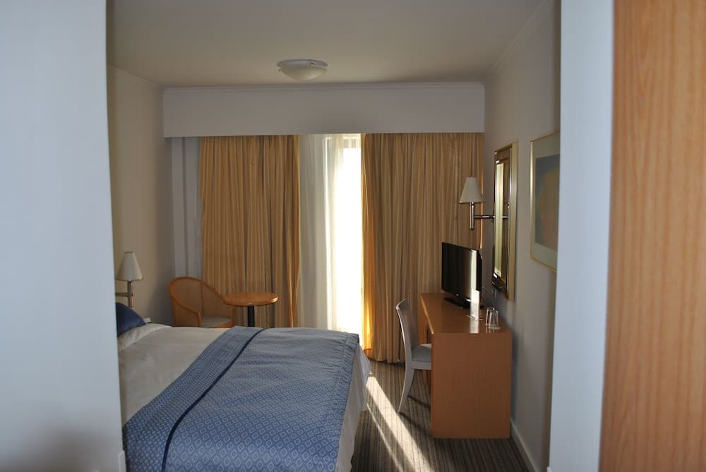A cozy hotel room with warm curtains, a neatly made bed, a desk with a TV, and soft lighting creates an inviting atmosphere ideal for travelers seeking comfort and relaxation.