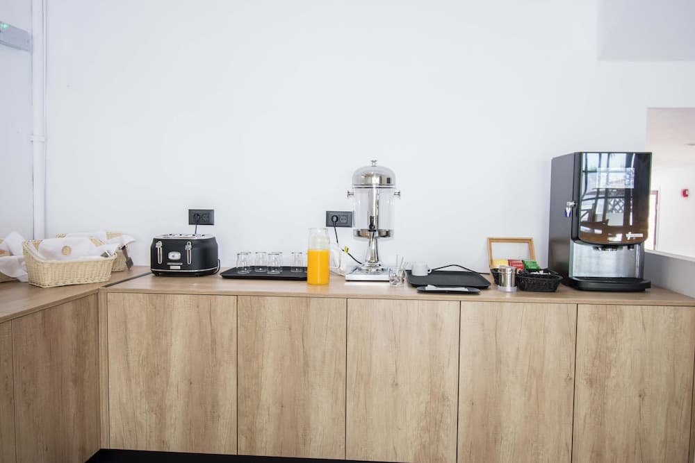 A cozy office breakroom features a wooden counter with a toaster, coffee maker, juice dispenser, and neatly arranged baskets, ideal for travelers seeking a comfortable workspace or meeting spot.