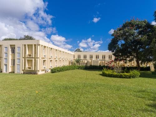 A serene hotel complex with lush green lawns, blooming trees, and a clear blue sky offers a tranquil retreat for travelers seeking relaxation and comfort.