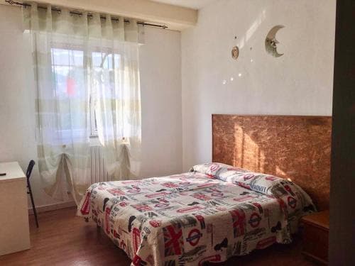 A cozy bedroom with a bed adorned in a vibrant London-themed duvet, soft curtains by the window, and a wooden headboard, ideal for travelers seeking a comfortable and stylish accommodation.