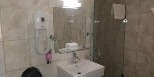 A clean, modern bathroom with tiled walls, a glass shower enclosure, a wall-mounted hairdryer, and a sink with a mirror above it, ideal for travelers seeking comfort and convenience in their accommodations.