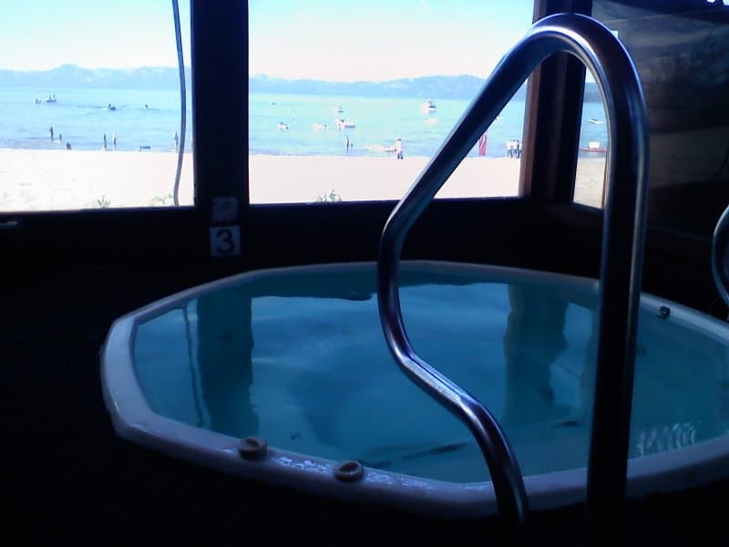 A serene indoor hot tub offers a relaxing view of a bustling beach and tranquil waters, ideal for travelers seeking a peaceful retreat with ocean vistas.