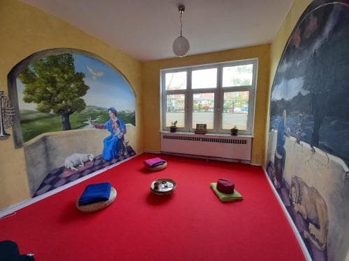 A serene meditation room with vibrant red carpet, calming murals depicting nature scenes, and cozy cushions invites travelers seeking relaxation and mindfulness practices.