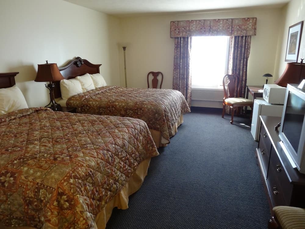 A cozy hotel room features two patterned beds, a desk by the window, and a TV on a dresser, ideal for travelers seeking comfort and functionality.