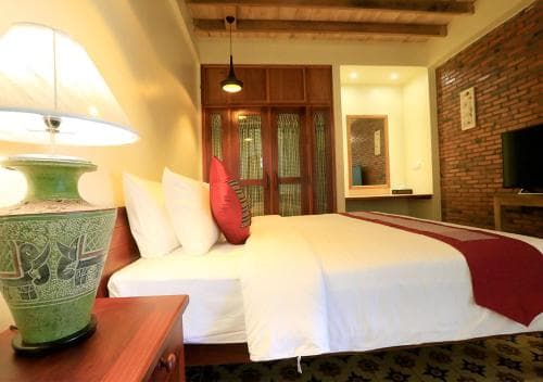 A cozy hotel room with warm lighting, wooden furnishings, a brick wall accent, and decorative pillows creates an inviting atmosphere ideal for travelers seeking comfort and relaxation.