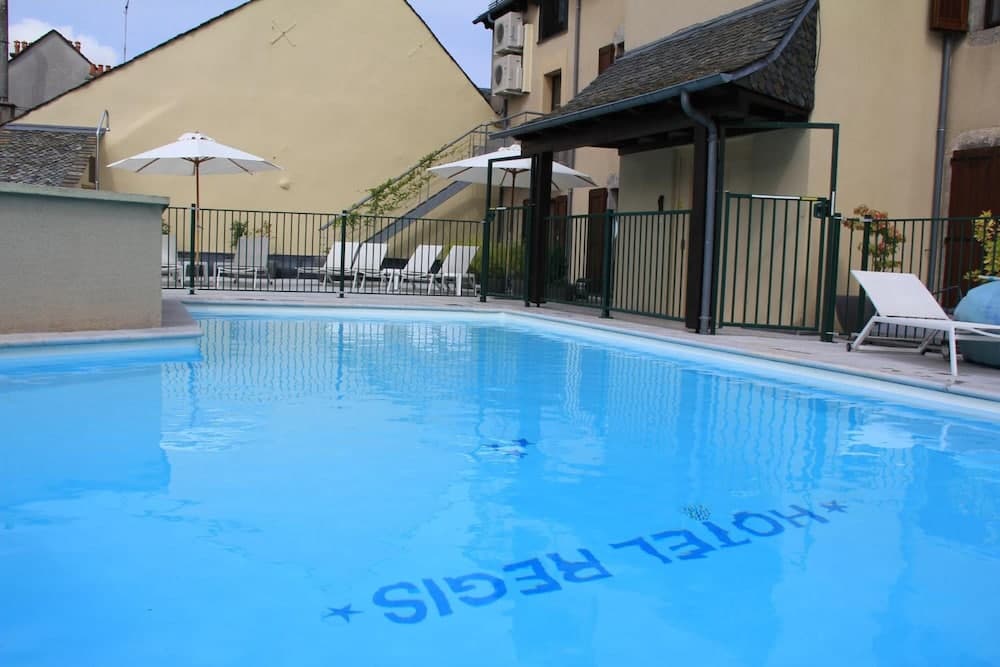 A serene outdoor pool area with lounge chairs, umbrellas, and a tiled patio invites relaxation at a charming hotel setting, perfect for travelers seeking a peaceful retreat.