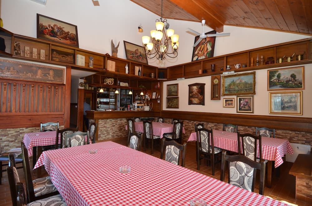 A cozy restaurant interior with wooden accents, red-checkered tablecloths, framed artwork, and warm lighting creates an inviting atmosphere perfect for travelers seeking a traditional dining experience.
