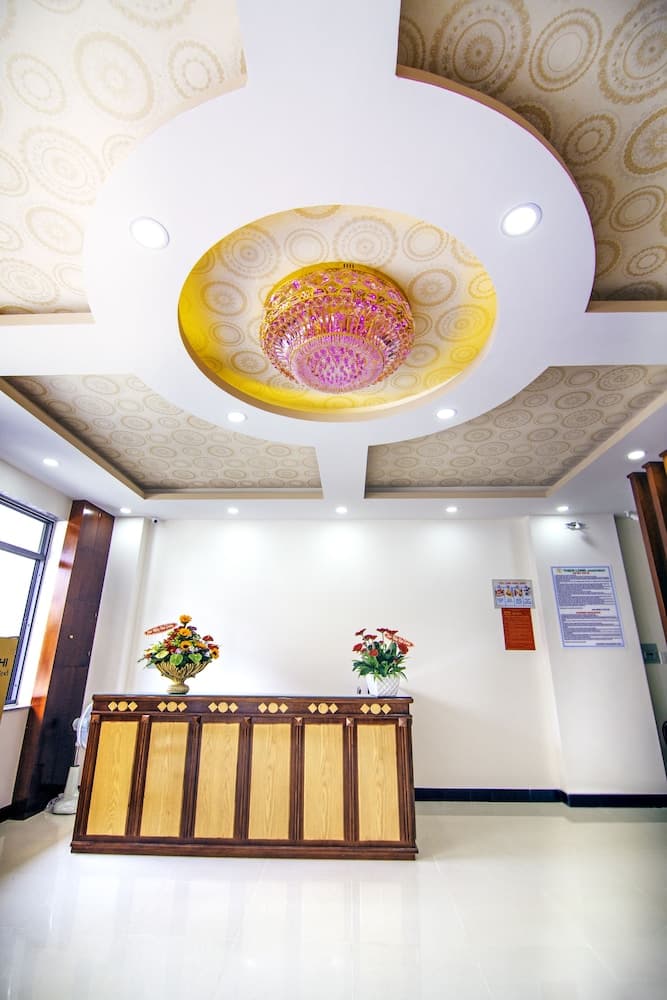 A warmly lit hotel lobby features a wooden reception desk adorned with floral arrangements under an ornate ceiling light, creating a welcoming atmosphere ideal for travelers seeking comfort and elegance.