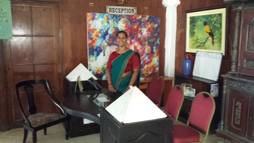 A warmly lit reception area features wooden furnishings, vibrant artwork, and a welcoming hostess in traditional attire, ideal for travelers seeking a cozy and culturally rich accommodation experience.