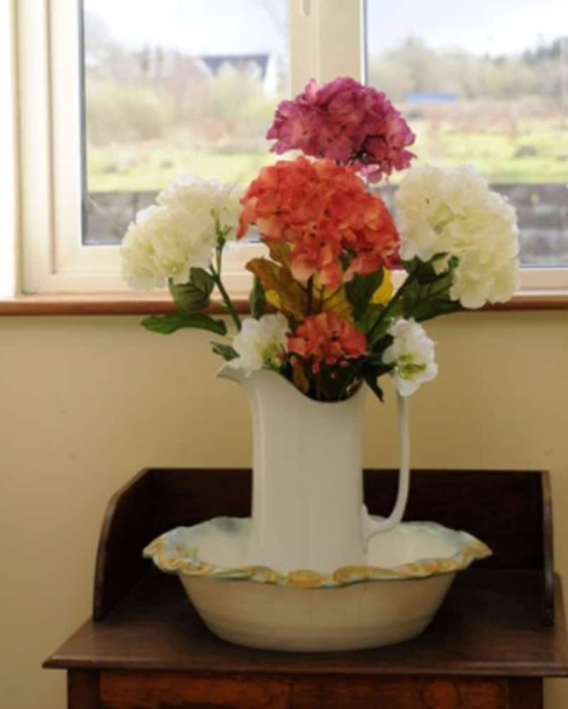 A cozy indoor setting features vibrant hydrangeas in a white pitcher atop a wooden table by a window overlooking a serene countryside, ideal for travelers seeking a tranquil retreat.