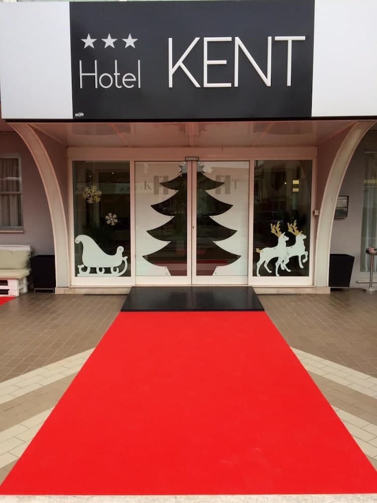 A festive entrance to the Hotel Kent features a red carpet leading to glass doors adorned with Christmas tree and reindeer decals, creating a welcoming holiday atmosphere ideal for seasonal travelers seeking cozy accommodations.