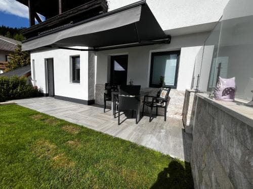 A serene modern patio with lounge chairs under a black awning invites relaxation in a tranquil suburban setting, perfect for travelers seeking a peaceful retreat.