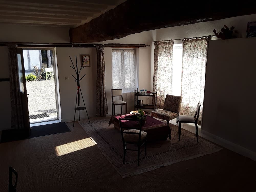 A cozy living room with rustic wooden beams, floral curtains, and soft sunlight filtering through the windows creates an inviting atmosphere ideal for a relaxing getaway.