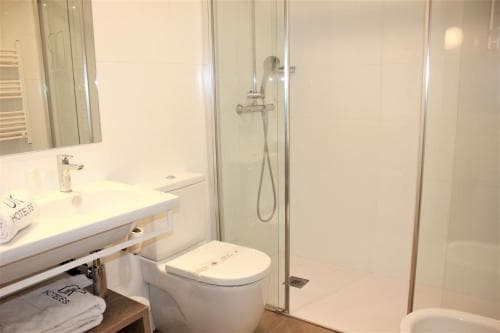 A clean, modern bathroom featuring a sleek glass shower enclosure, white fixtures, and neatly folded towels, ideal for travelers seeking comfort and hygiene in their accommodations.