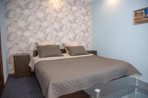 A cozy hotel room features a neatly made bed with gray bedding against a patterned wall, creating a serene atmosphere ideal for travelers seeking comfort and relaxation.