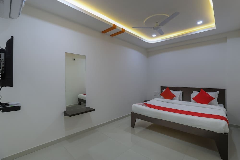 A cozy hotel room with a neatly made bed adorned in red and white linens, a wall-mounted TV, a ceiling fan, and soft ambient lighting creates a welcoming atmosphere ideal for travelers seeking comfort and relaxation.