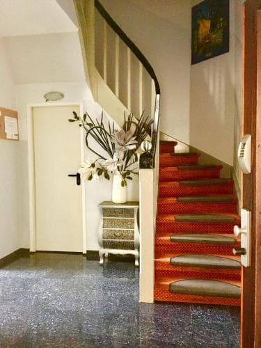 A cozy hotel lobby features a vibrant red-carpeted staircase, a decorative vase with plants on a side table, and warm lighting, creating an inviting atmosphere ideal for travelers seeking comfort and charm.