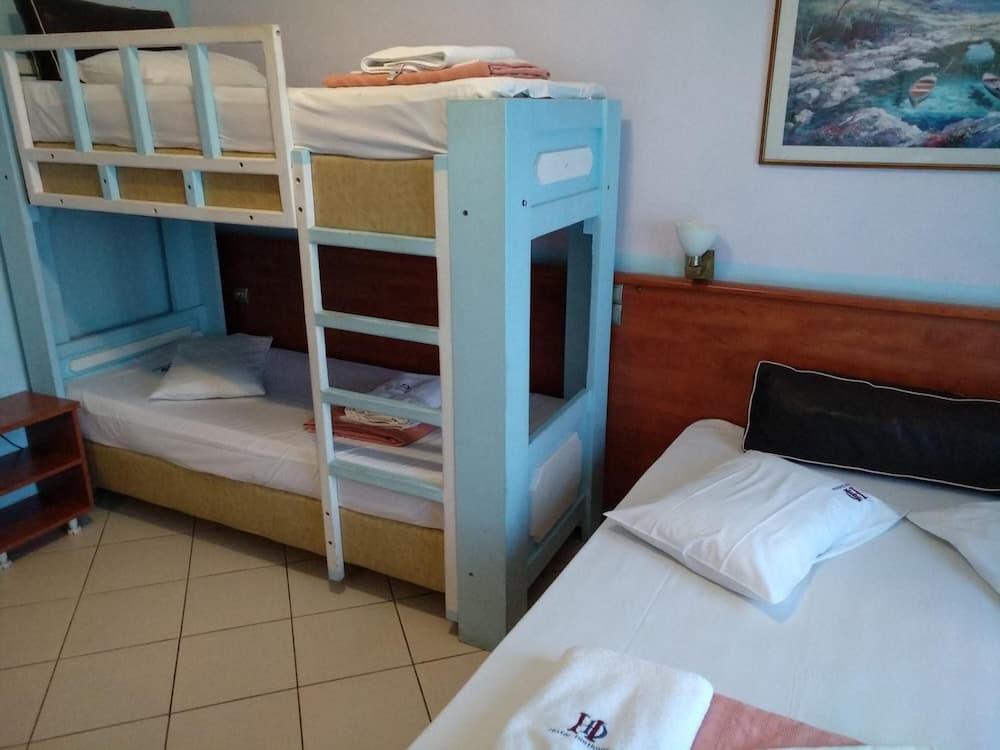 A cozy hostel room features a blue bunk bed and single bed with neatly arranged towels, set against a serene backdrop with a wall-mounted lamp and artwork, ideal for budget travelers seeking comfort.