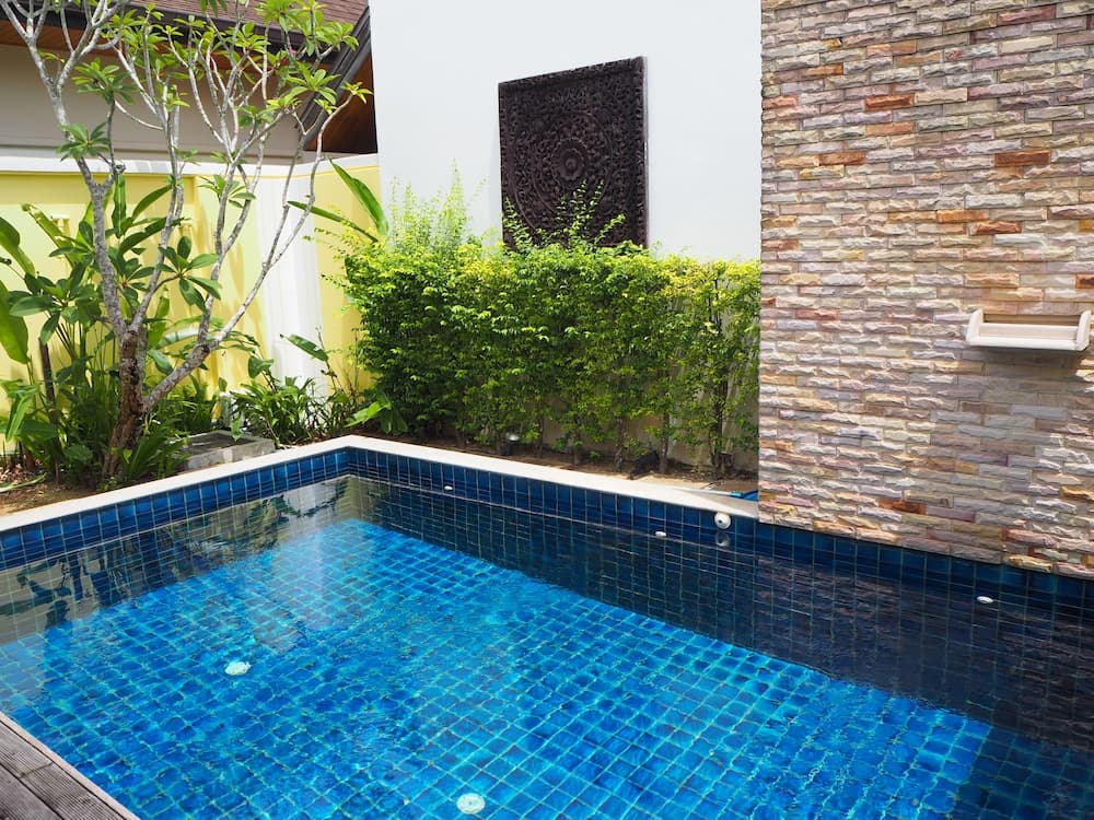 A serene private pool surrounded by lush greenery and a textured stone wall, featuring vibrant blue tiles and decorative elements, ideal for a relaxing tropical getaway.