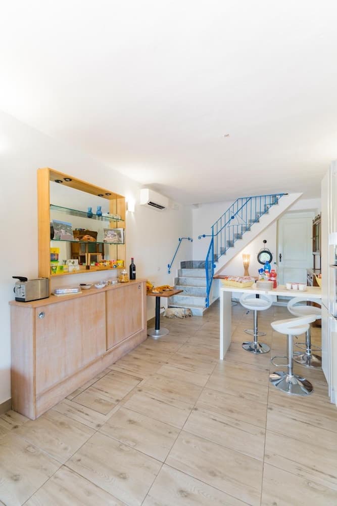 A cozy kitchenette with wooden flooring, a wooden cabinet adorned with shelves of colorful items, a staircase with blue railings leading upstairs, and a modern bar area with stools creates an inviting atmosphere ideal for travelers seeking a comfortable self-catering accommodation.