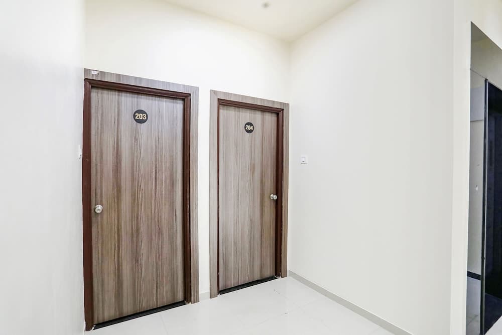 A clean, minimalist hotel corridor with numbered wooden doors and white walls offers a serene atmosphere ideal for travelers seeking simple accommodations.