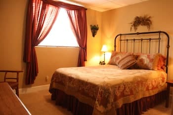 A cozy bedroom with warm yellow walls, red curtains framing a bright window, and a vintage iron bed adorned with patterned bedding creates an inviting atmosphere, perfect for travelers seeking a comfortable and charming accommodation.