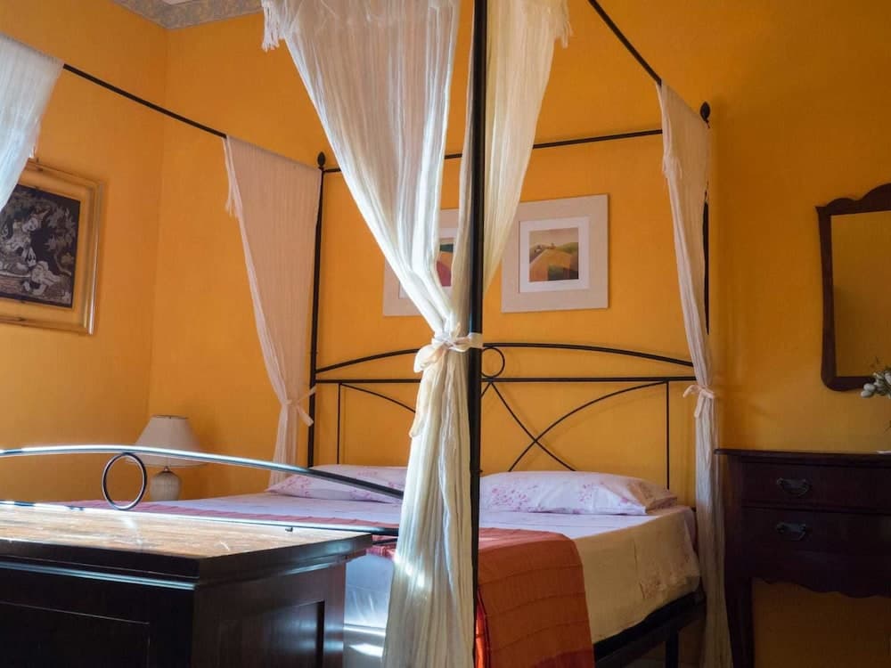 A cozy bedroom with vibrant yellow walls, a canopy bed adorned with flowing white curtains, and classic furnishings creates an inviting atmosphere ideal for travelers seeking a warm and charming accommodation experience.