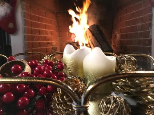 A cozy fireplace scene adorned with festive red berries, golden ornaments, and white candles creates a warm, inviting holiday atmosphere perfect for winter travel inspiration.