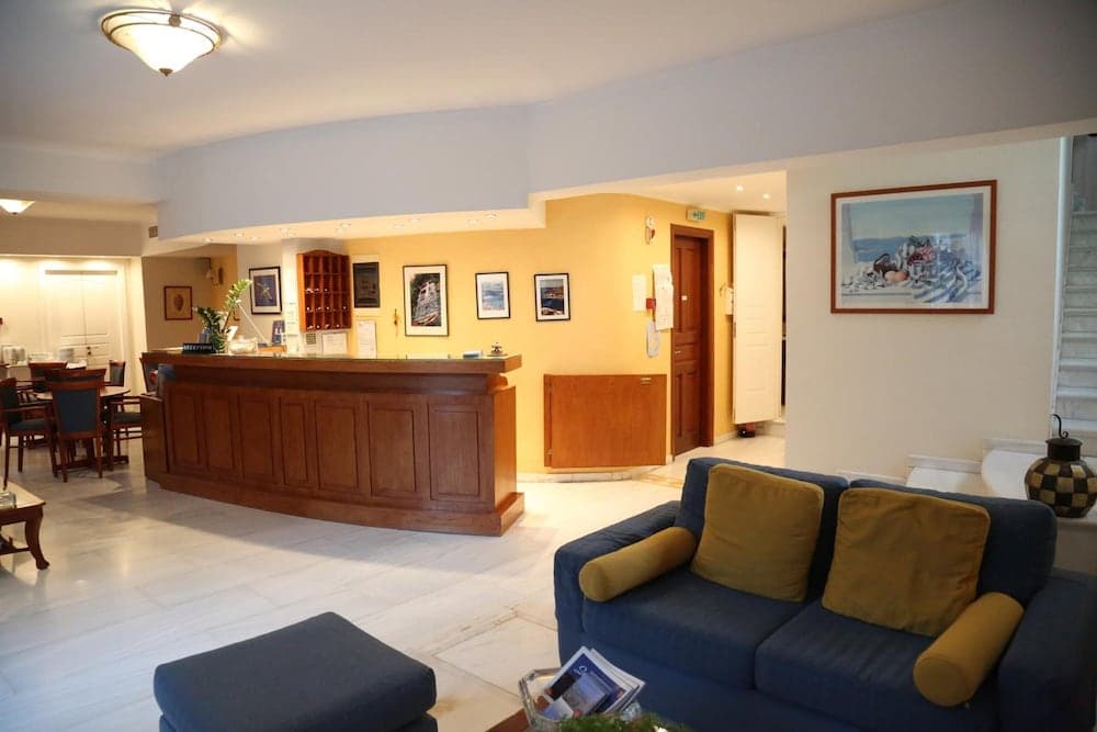 A cozy hotel lobby features a wooden reception desk, comfortable blue sofas with yellow cushions, framed artwork on the walls, and a warm ambiance ideal for travelers seeking relaxation and hospitality.