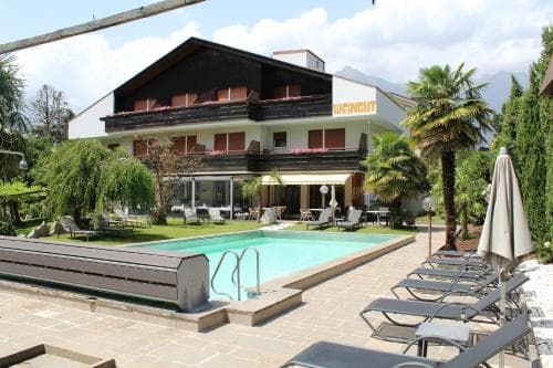 A serene hotel courtyard features a sparkling pool surrounded by lounge chairs and lush greenery, ideal for travelers seeking relaxation in a picturesque mountain retreat.
