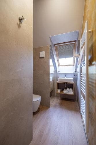 A modern bathroom with wooden flooring, sleek fixtures, and natural light from a window creates a serene atmosphere, ideal for travelers seeking comfort and style in their accommodations.