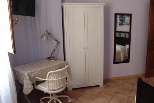 A cozy hotel room corner features a white desk chair, patterned tablecloth, and armoire against lavender walls, creating a serene workspace ideal for travelers seeking comfort and functionality.