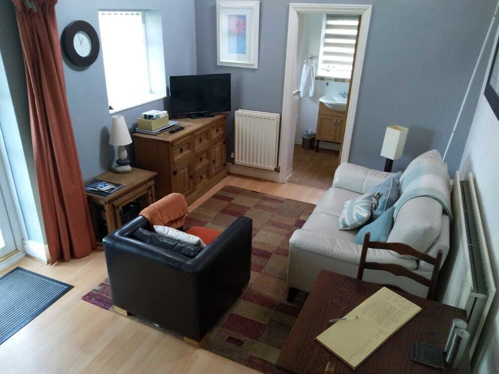 A cozy living room with soft furnishings, wooden floors, and a view into an adjacent bathroom creates a welcoming atmosphere ideal for travelers seeking a comfortable and homey accommodation.