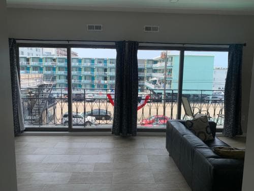 A cozy living room with a tiled floor and a large balcony offers a vibrant beachside view, perfect for travelers seeking relaxation and proximity to the oceanfront amenities.