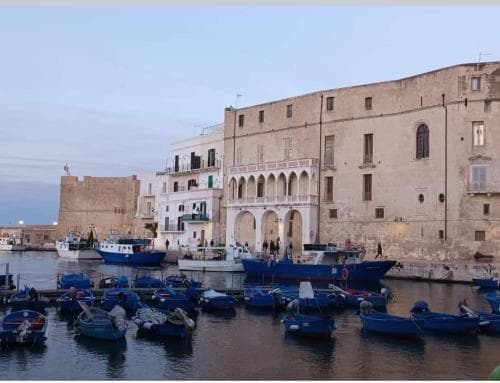 A serene harbor scene features small blue boats docked near historic stone buildings under a calm sky, ideal for travelers seeking cultural exploration and maritime charm.