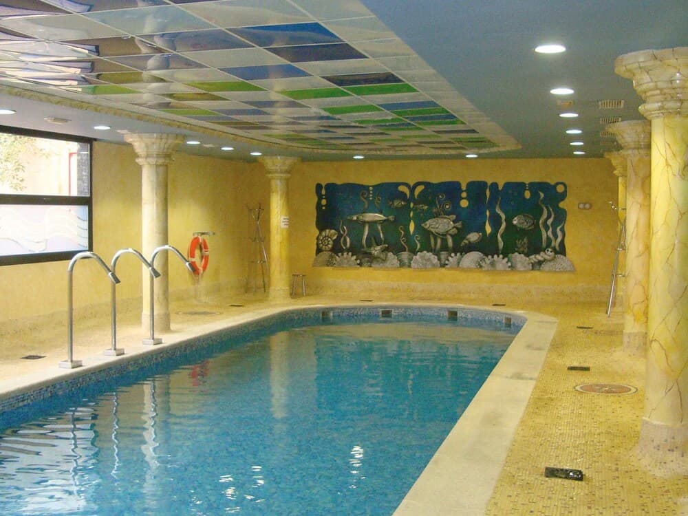 A serene indoor pool area features a vibrant mural of sea life on the wall, surrounded by elegant columns and a mosaic-tiled floor, ideal for relaxation and leisure activities.
