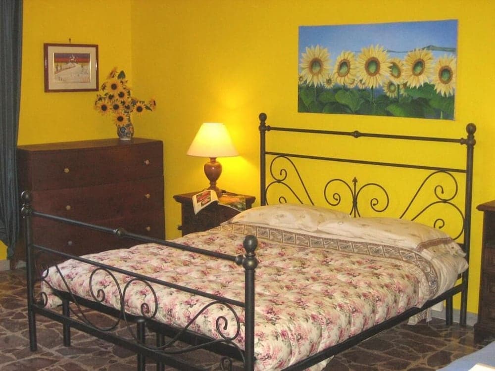 A cozy bedroom with vibrant yellow walls, a floral-patterned bedspread, and sunflower artwork creates a cheerful and inviting atmosphere, ideal for travelers seeking a warm and artistic retreat.