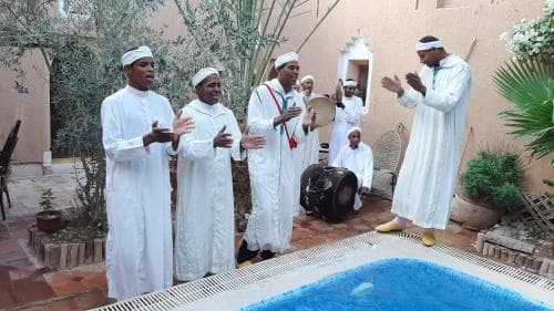 A serene courtyard with a pool features individuals in traditional white attire performing music, creating a tranquil cultural experience ideal for travelers seeking authentic local performances.