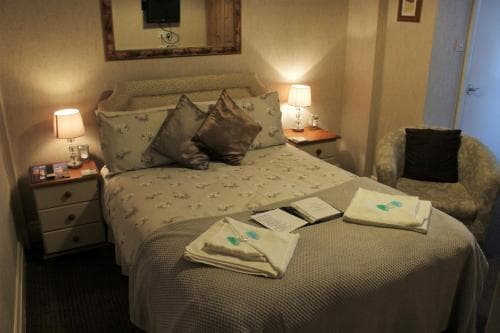 A cozy hotel room features a neatly made bed adorned with folded towels and reading materials, flanked by bedside tables with lamps, creating a warm and inviting atmosphere ideal for travelers seeking comfort and relaxation.