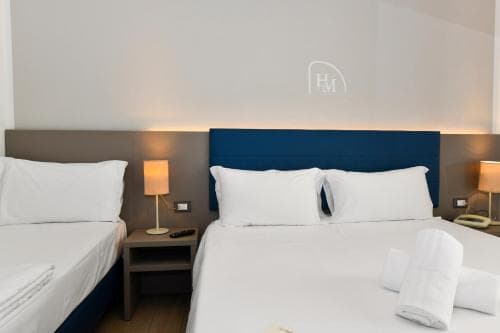A cozy hotel room features two neatly made beds with white linens, blue headboards, and warm bedside lamps, creating a welcoming atmosphere ideal for travelers seeking comfort and relaxation.