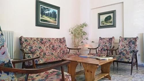 A cozy living room with floral-patterned furniture, framed landscape paintings, and a wooden coffee table creates a warm and inviting atmosphere, ideal for travelers seeking a comfortable and homely accommodation experience.