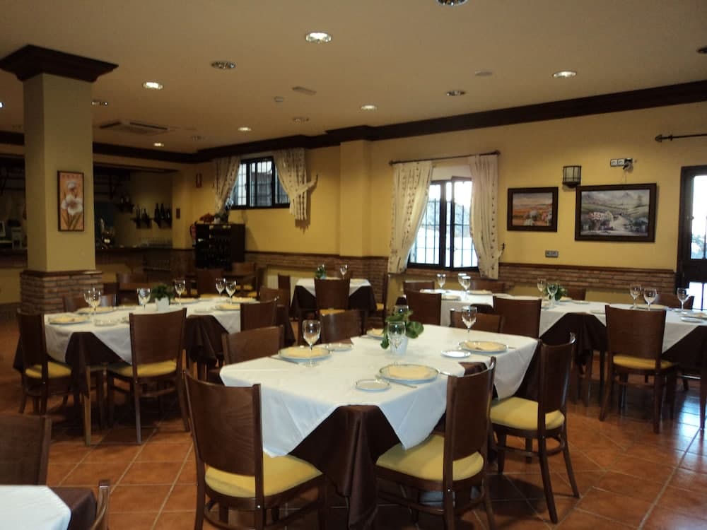 A cozy restaurant dining room with warm yellow walls, wooden tables set for guests, framed artwork, and large windows draped with curtains, ideal for a relaxing meal or group gathering.