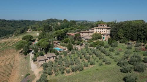A serene Tuscan countryside scene features a historic villa surrounded by lush olive groves, vineyards, and a tranquil pool, ideal for a luxurious retreat or romantic getaway.