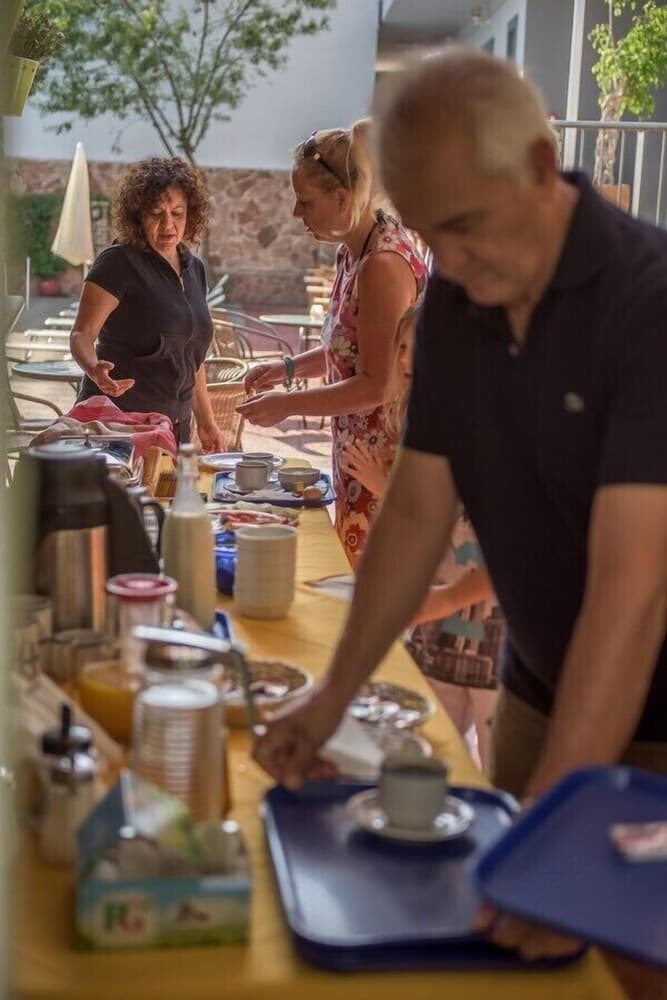 A lively outdoor café scene captures guests enjoying a buffet breakfast with coffee pots, juice, and assorted dishes, ideal for travelers seeking a cozy morning dining experience.
