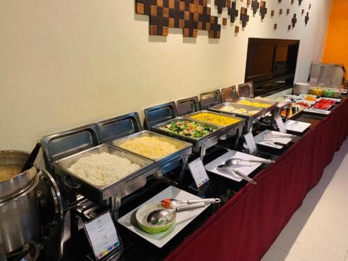 A vibrant buffet spread featuring rice, vegetables, and scrambled eggs on a sleek metal serving line in a modern dining area, ideal for travelers seeking convenient meal options at hotels or resorts.